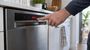 A technician's hand pointing at an unreadable glowing fault code on a built-in dishwasher's control display
